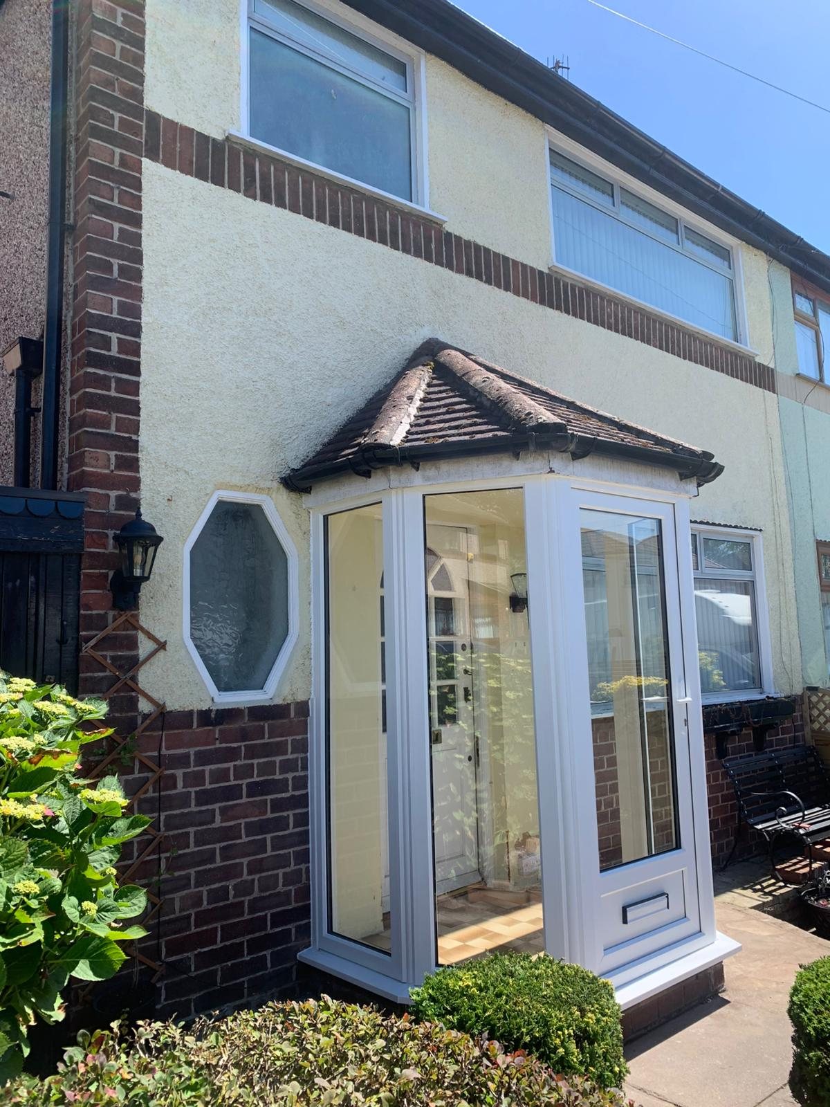 A white glazed corner porch with a front door on a semi-detached house