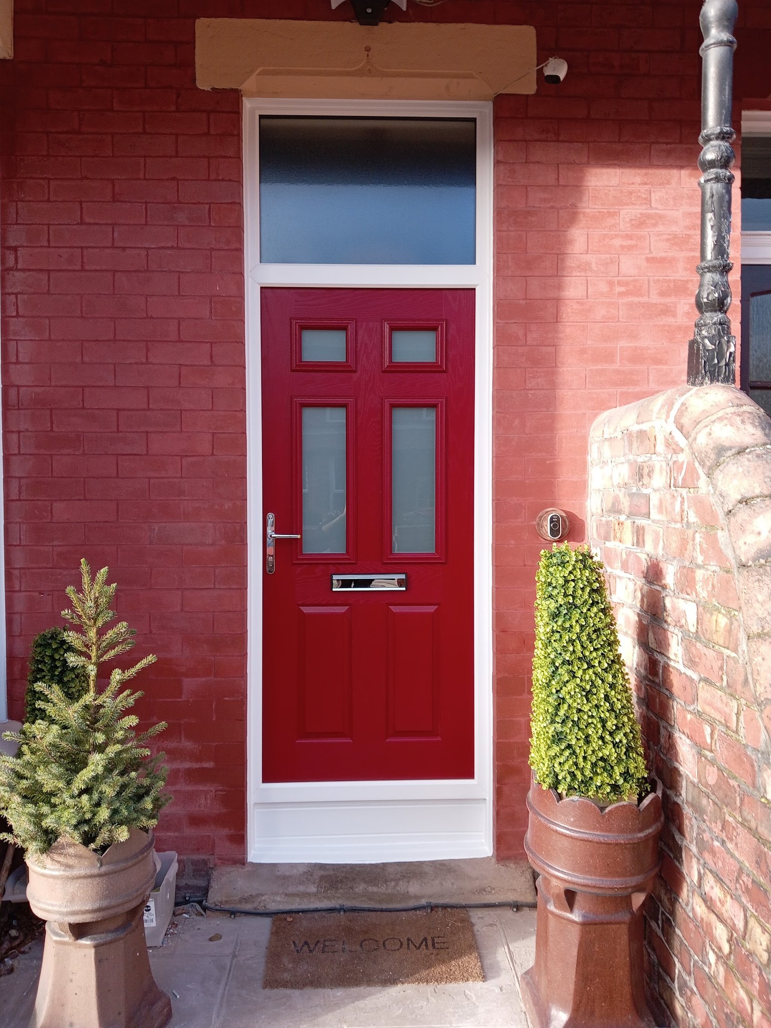 A red front door with a glazed top light, set in a red-painted brick wall