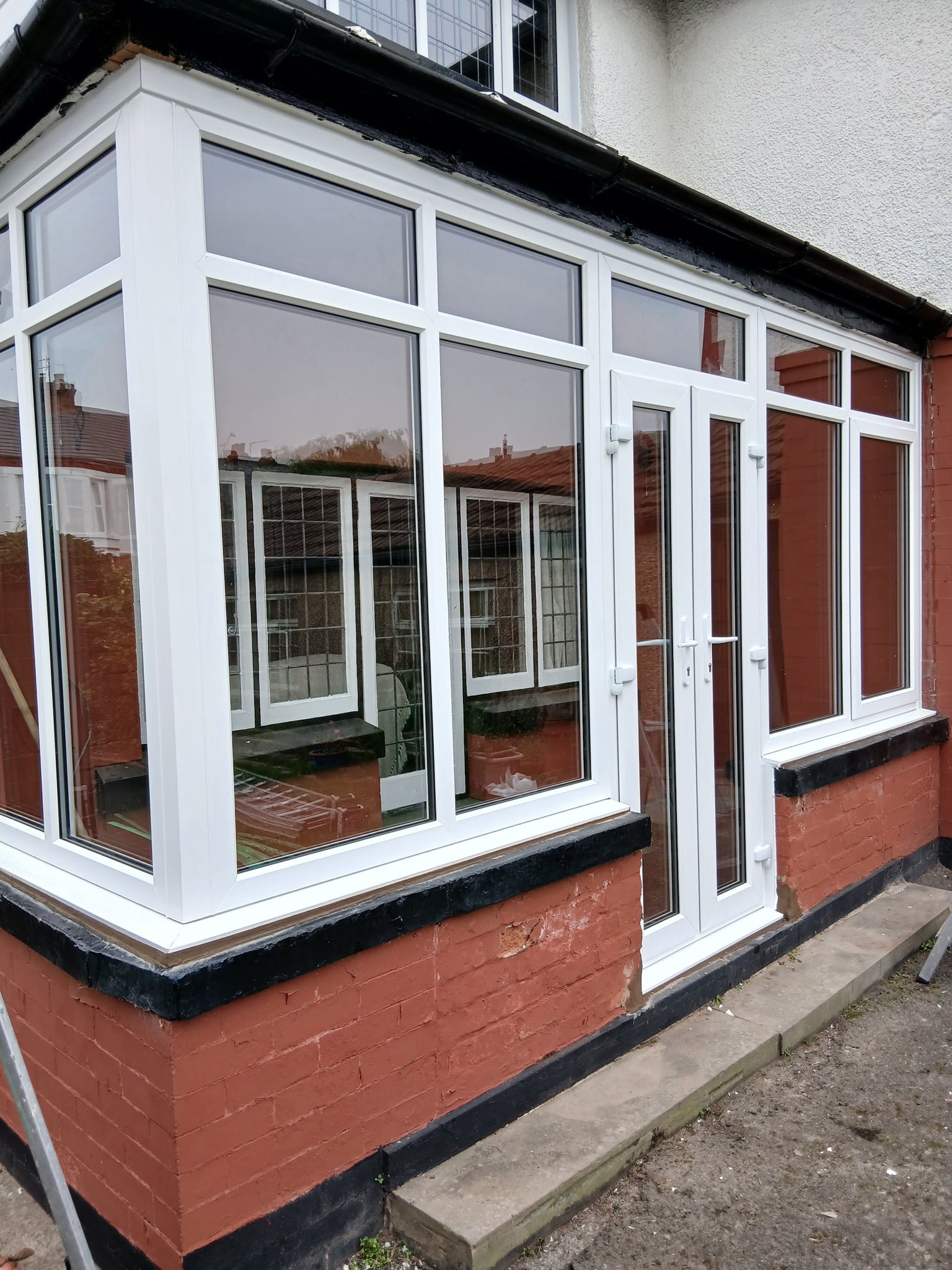 A white glazed front extension on a red-painted brick house, seen from the side